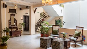 A spacious lobby with a staircase, potted plants, a wooden chair, and a large mirror. - Udaigarh (Udaipur)