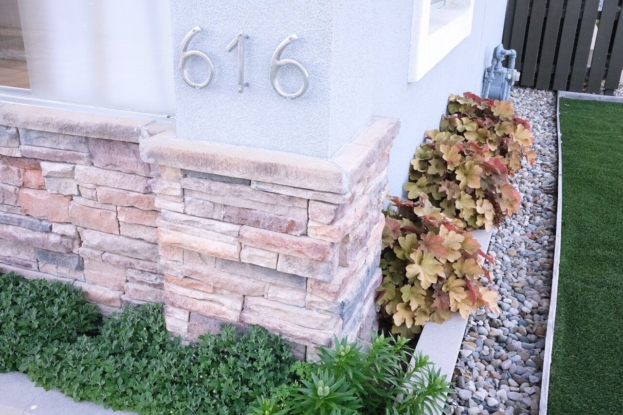 A house number 616, stone wall, and a planter with autumn leaves.