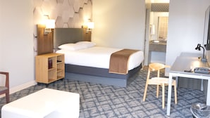 A hotel room with a bed, bedside tables, a desk, a chair, and a bathroom visible through an open door. - Regency Inn (Eddyville)