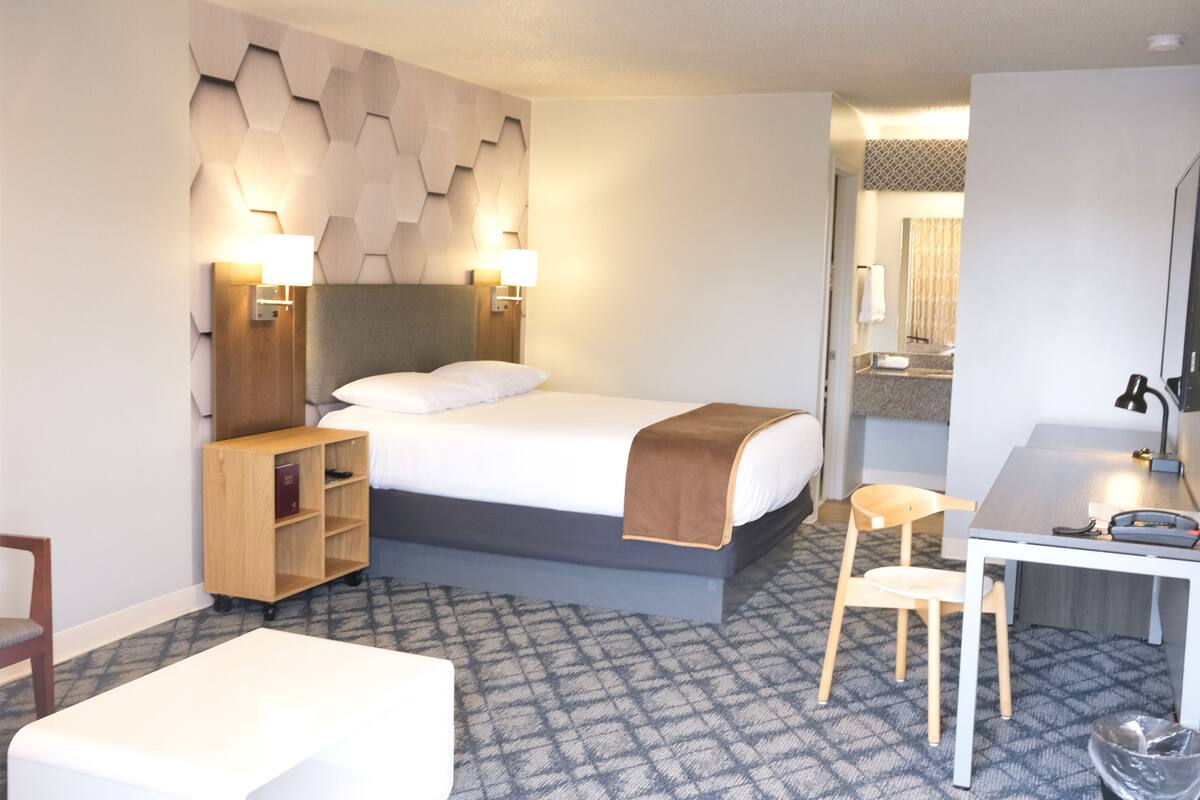 A hotel room with a bed, bedside tables, a desk, a chair, and a bathroom visible through an open door.