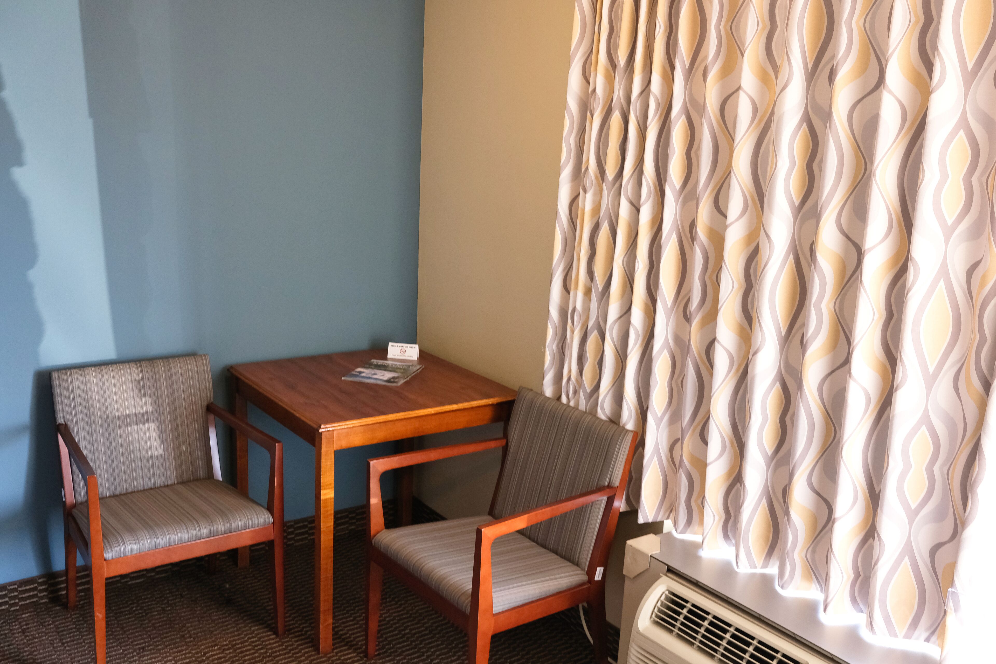 A room with two wooden chairs, a small table, and a patterned curtain.