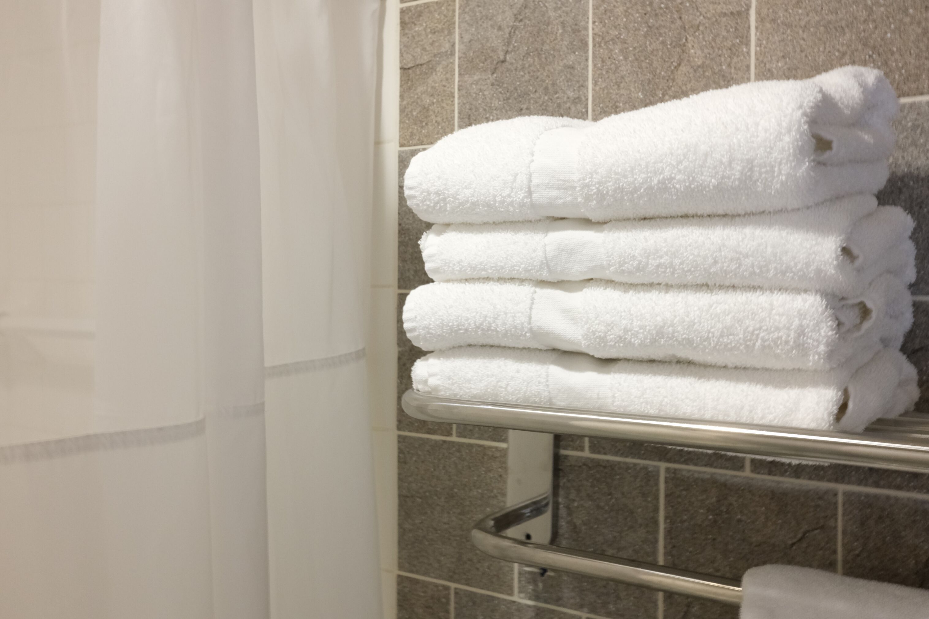 Un montón de toallas blancas sobre un escurreplatos metálico en un baño con paredes de azulejos.