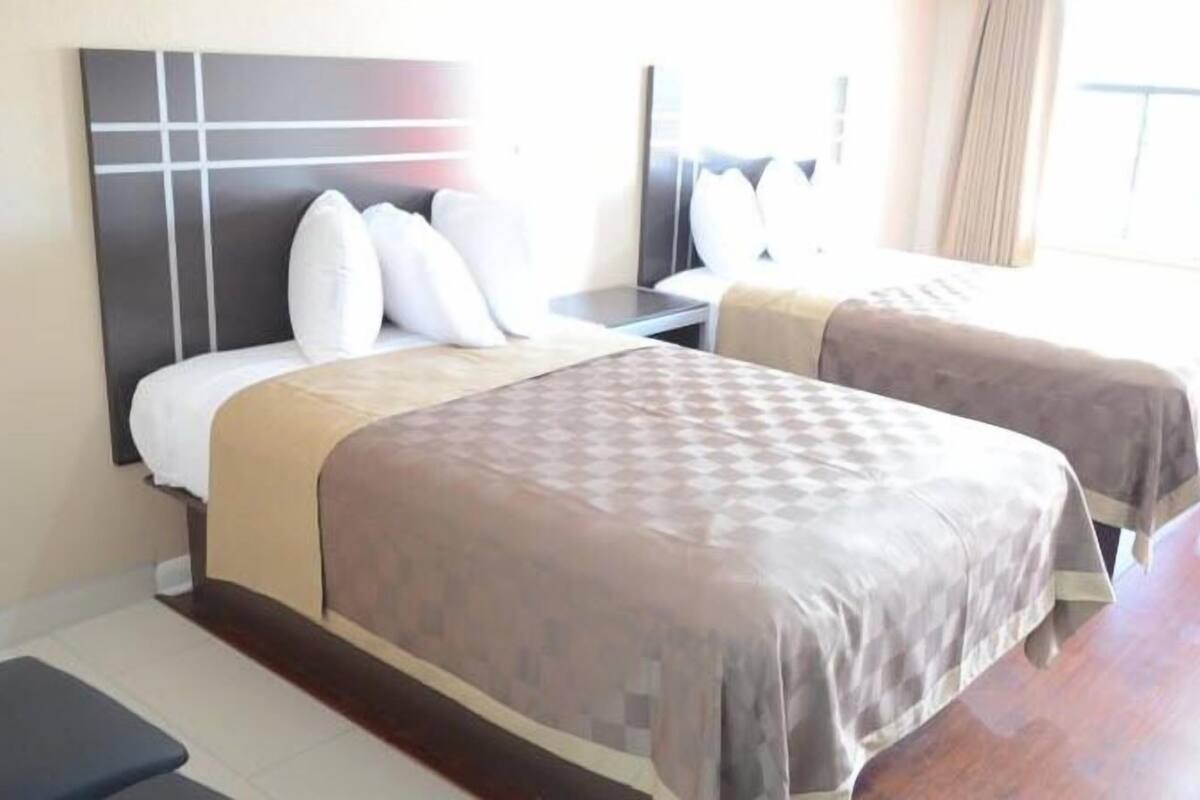 A hotel room with two beds, a nightstand, and a window with curtains.