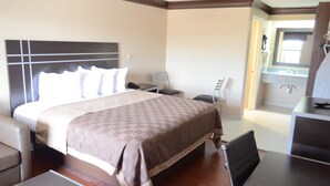 Ein Hotelzimmer mit einem großen Bett, einem Schreibtisch, einem Stuhl und einem durchgegangenen Türrahmen sichtbaren Badezimmer.