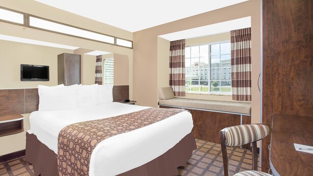 A hotel room with a large bed, a desk, a chair, a television, and a window with curtains. - Microtel Inn & Suites by Wyndham Mansfield (Mansfield)