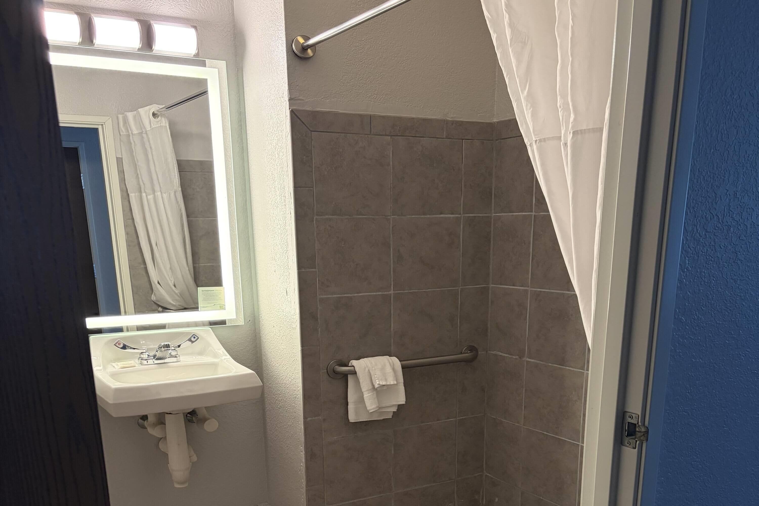 A bathroom with a sink, mirror, shower, and towel rack.