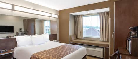 A hotel room with a large bed, a flat-screen TV, a desk with a telephone, a window with a view of the city, and a kitchenette area.