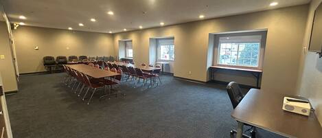 A conference room with multiple tables and chairs, carpeted floor, and windows with views.