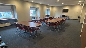 A conference room with multiple tables and chairs, large windows, and a flat-screen TV on the wall.