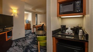 A hotel room with a kitchenette, a television, a desk with a computer, and a seating area with chairs.