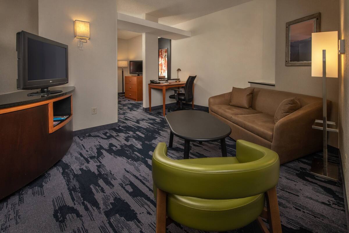 Ein Hotelzimmer mit Flachbildfernseher, Schreibtisch mit Stuhl, Sofa und Lampe.