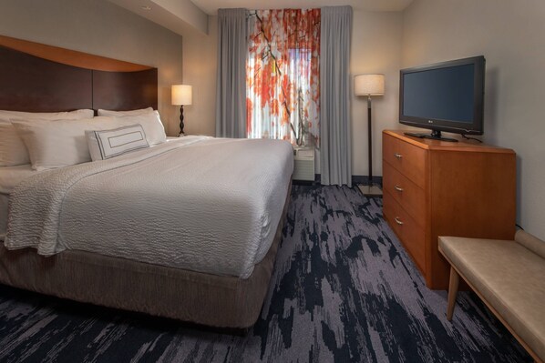 A hotel room with a large bed, a television on a wooden cabinet, and a desk with a lamp.