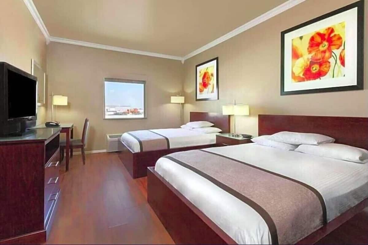 A hotel room with two beds, a desk, a chair, a TV, and a window with a view.
