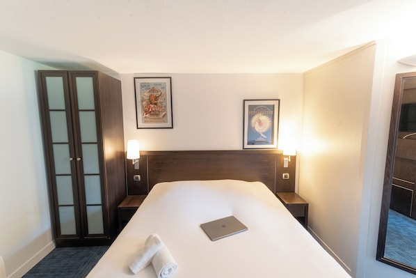 Habitación de hotel con una cama grande, un escritorio, un armario y dos lámparas de pared.
