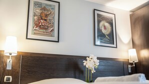 Ein Hotelzimmer mit einem hölzernen Kopfteil, zwei gerahmten Postern, einer Nachttischlampe und einer Vase mit weißen Blumen.