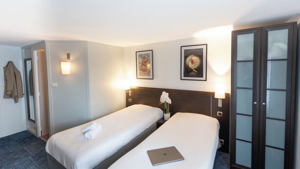 A hotel room with two beds, a laptop on the larger bed, a nightstand with a lamp, and a wardrobe with glass doors. - OUT Hotel In Nantes-Carquefou (Carquefou)