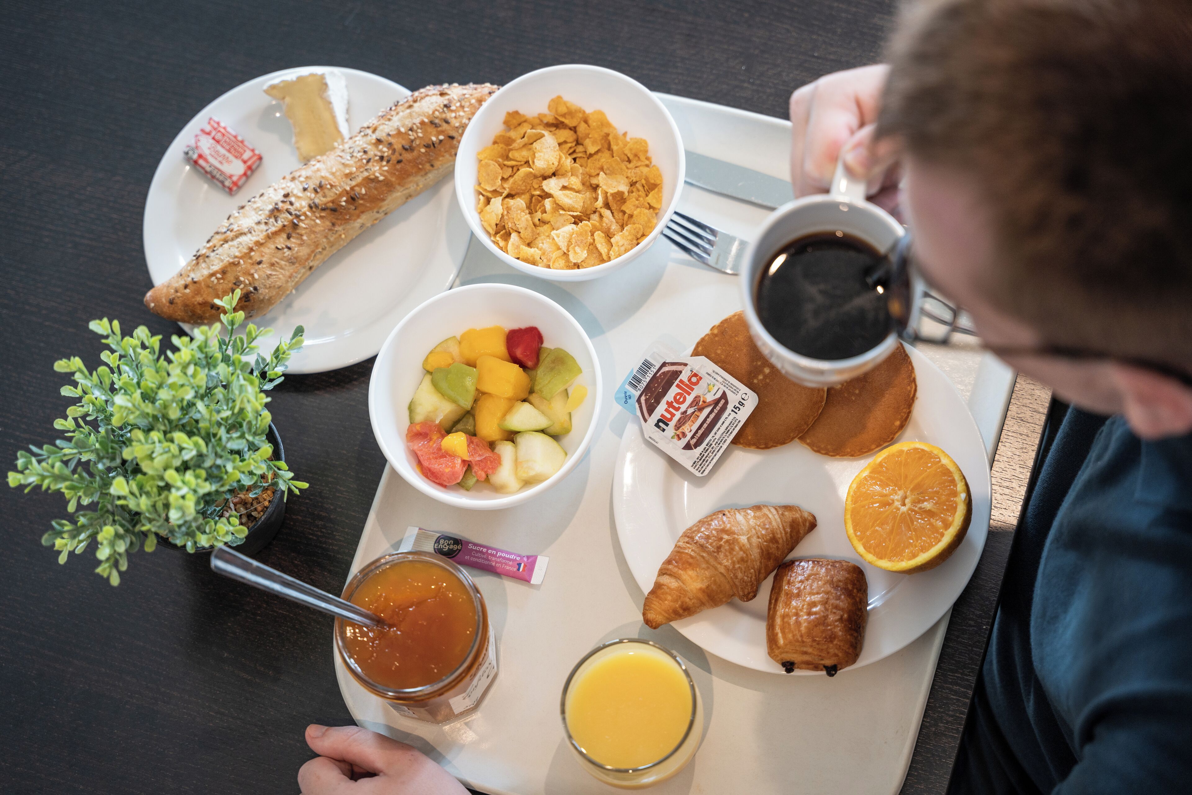 Un vassoio della colazione con croissant, cereali, frutta, caffè e succo di frutta.