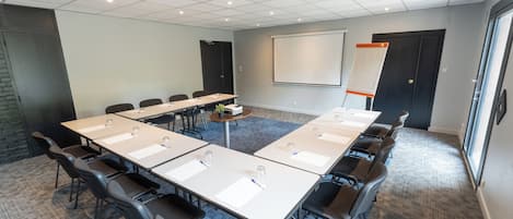 A conference room with a long table, chairs, a projector screen, and a whiteboard.