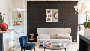 Ein modernes Wohnzimmer mit einer schwarzen Ziegelwand, einem grauen Sofa, einem Glastisch und einem blauen Sessel. Ein Glasvitrine beherbergt dekorative Gegenstände.