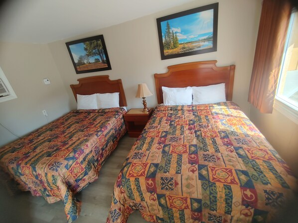A room with two beds, each with a patterned bedspread and white pillows. There is a painting on the wall above the beds and a window with curtains to the right. - Relax Inn Collingwood (Collingwood)