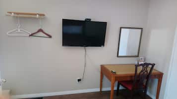 A room with a mounted television, a wooden desk, a chair, and a coat rack with hangers.