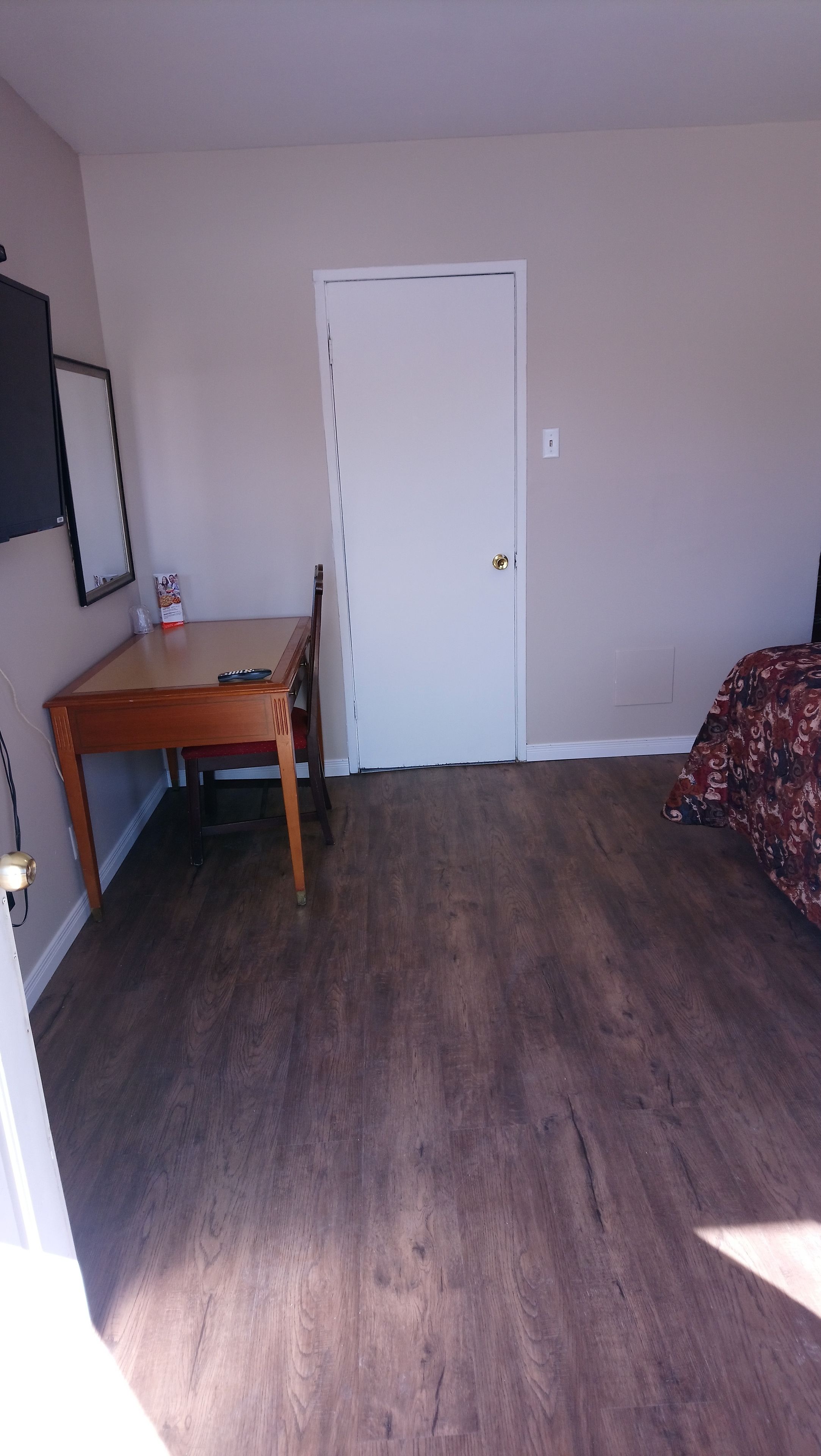 A room with a wooden desk, a bed with a patterned bedspread, and a white door.
