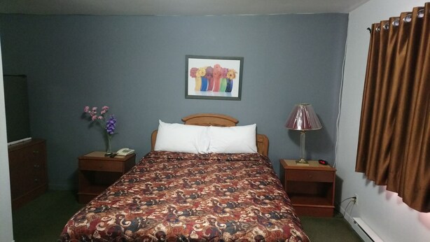 A bedroom with a bed, two nightstands, a lamp, a phone, and a painting on the wall. - Relax Inn Collingwood (Collingwood)