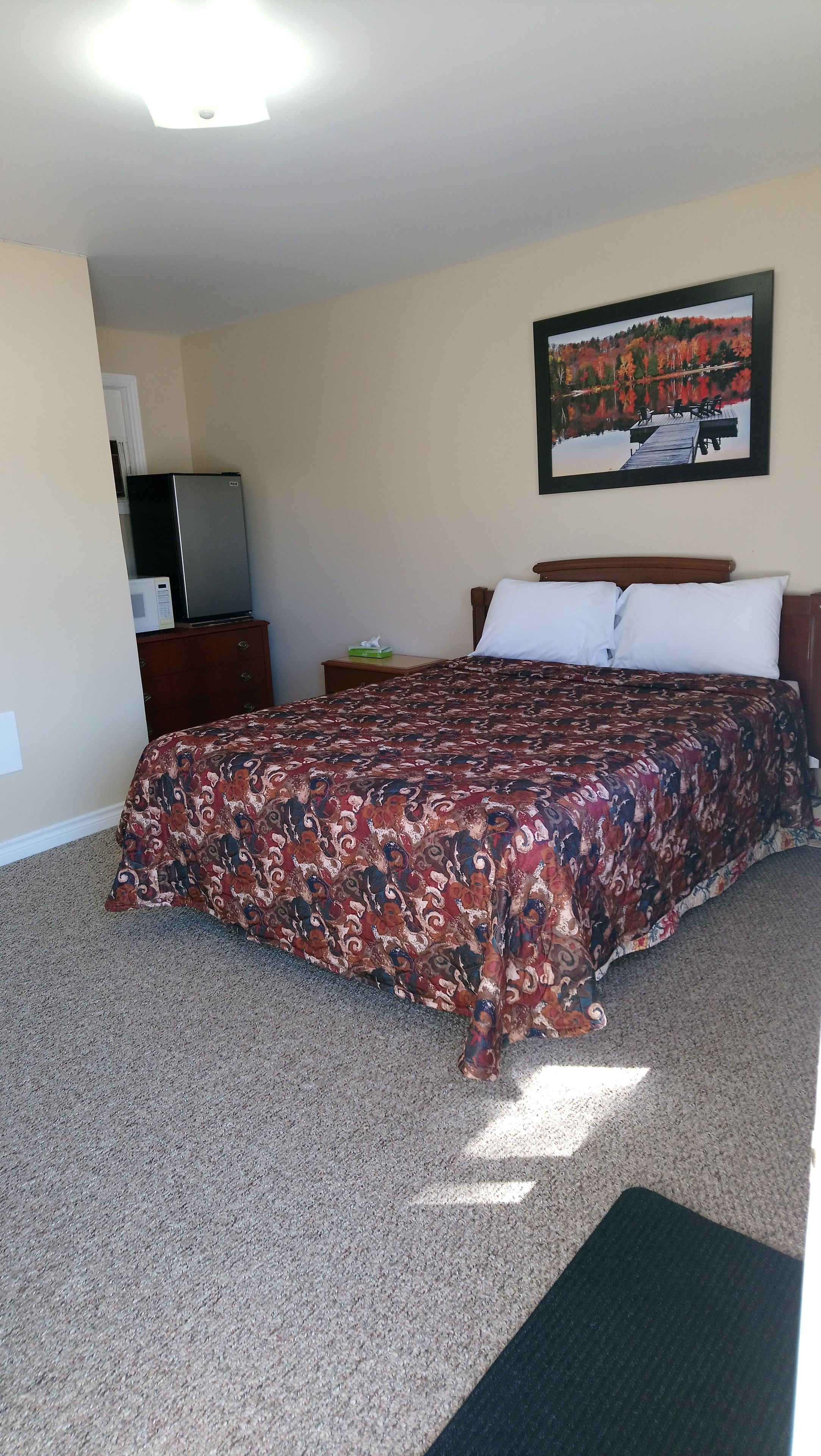A bedroom with a bed, a dresser, a nightstand, a painting, and a television.