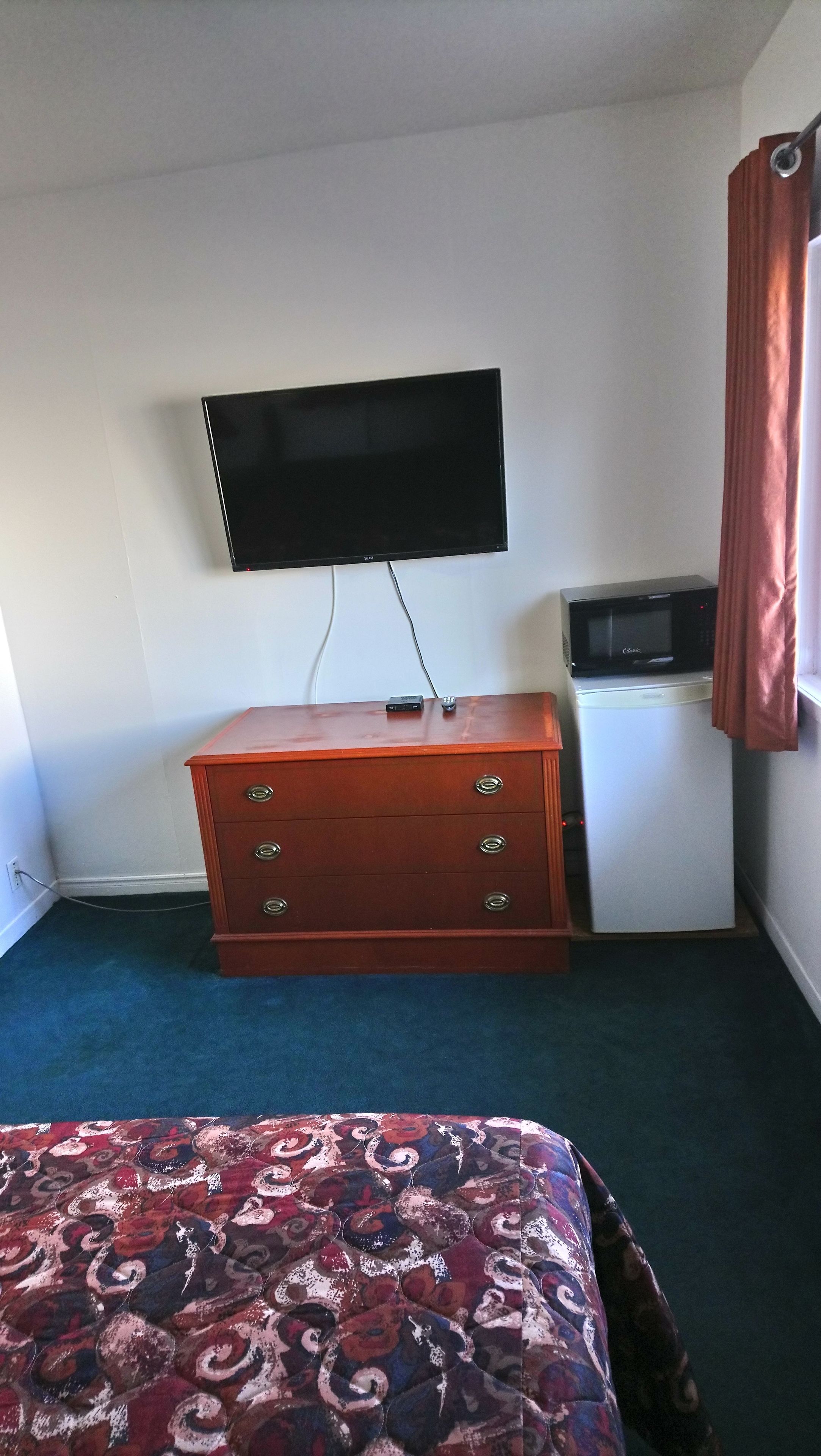 Una habitación de hotel con cama, cómoda, televisor y microondas.