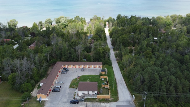 An aerial view of a motel with a parking lot, a small lawn, and a road leading to a forested area. - Relax Inn Collingwood (Collingwood)