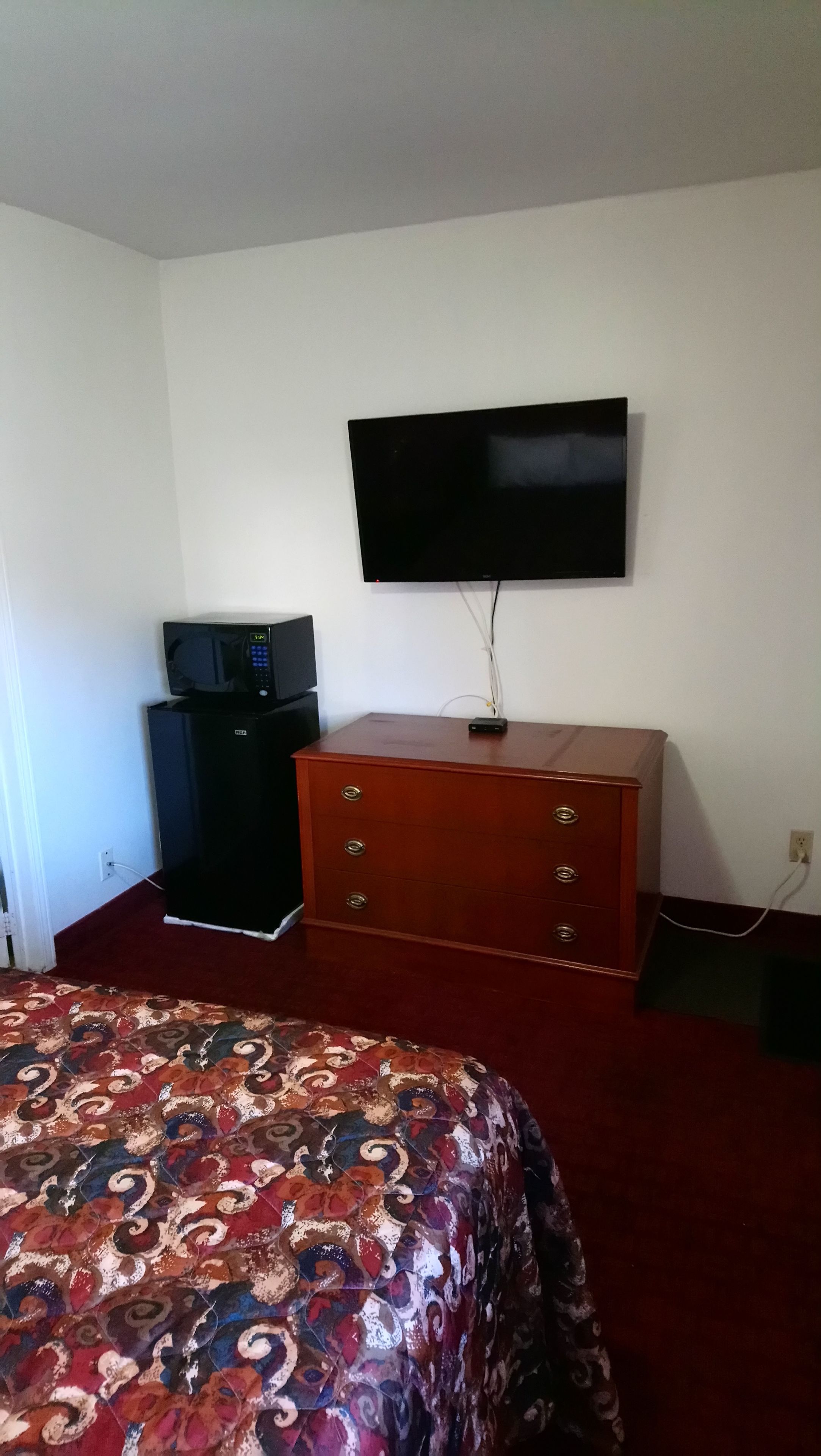 Quarto com cama, televisão na parede, micro-ondas e cómoda.