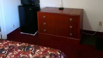 Quarto com cama, televisão na parede, micro-ondas e cómoda.
