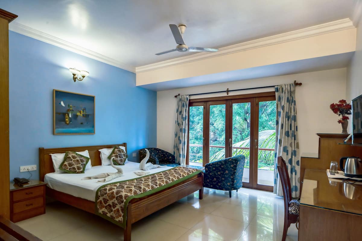 A hotel room with a bed, a desk, a chair, a ceiling fan, and a large window with curtains.