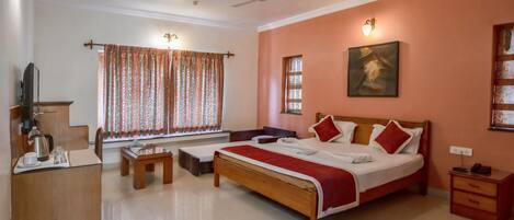 Habitación de hotel con cama, mesitas de noche, escritorio con silla, televisor y ventana con cortinas.