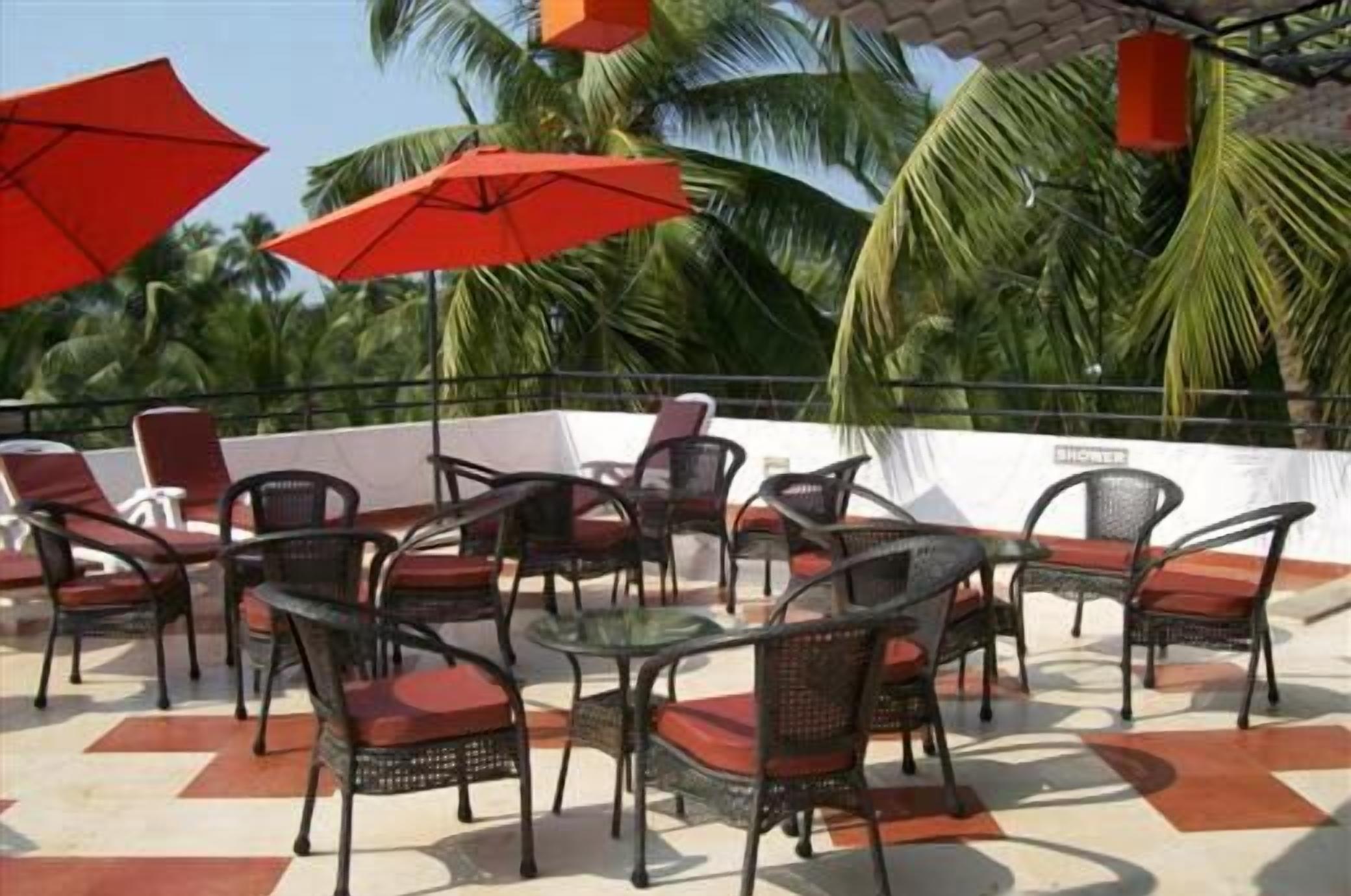 Un espacio al aire libre con sillas de mimbre y cojines rojos, rodeado de palmeras y sombrillas rojas.