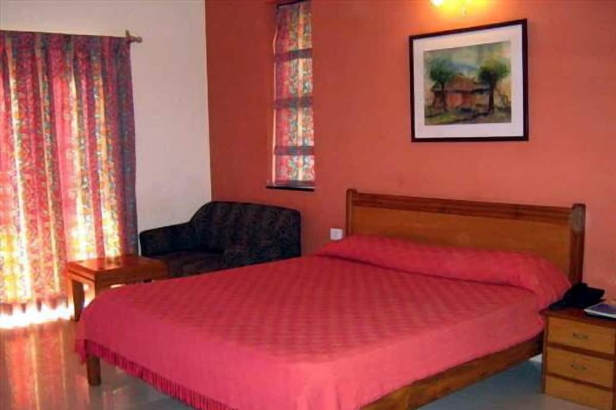 A bedroom with a wooden bed, a chair, a nightstand, a painting on the wall, and a window with curtains.