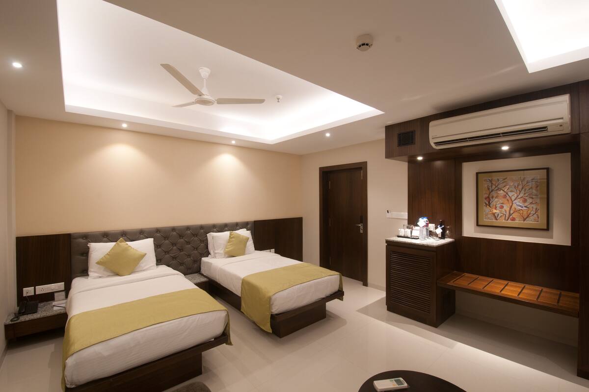 A hotel room with two beds, a ceiling fan, recessed lighting, an air conditioning unit, a bench, and a painting on the wall.
