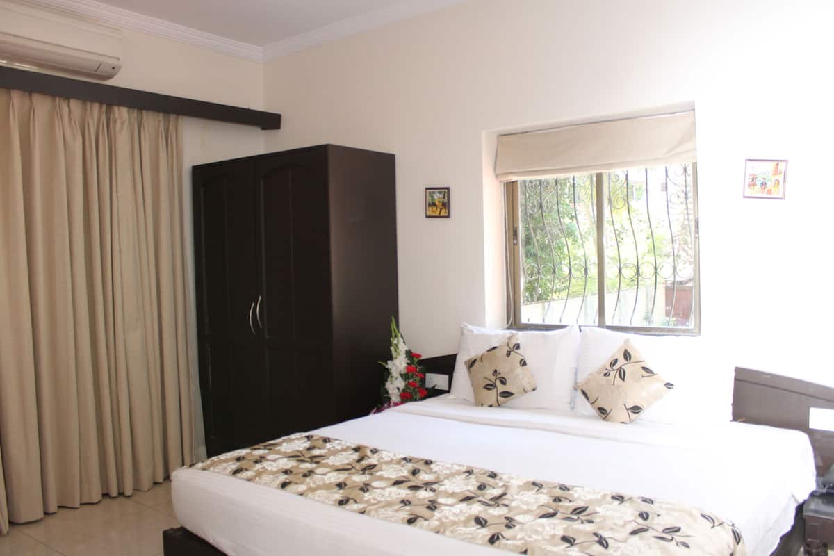A hotel room with a large bed, a wardrobe, a window with a view of greenery, and a small picture on the wall.