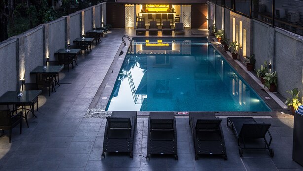 A poolside area with lounge chairs and tables, a bar, and a pool. - Hotel Calangute Towers (Calangute)