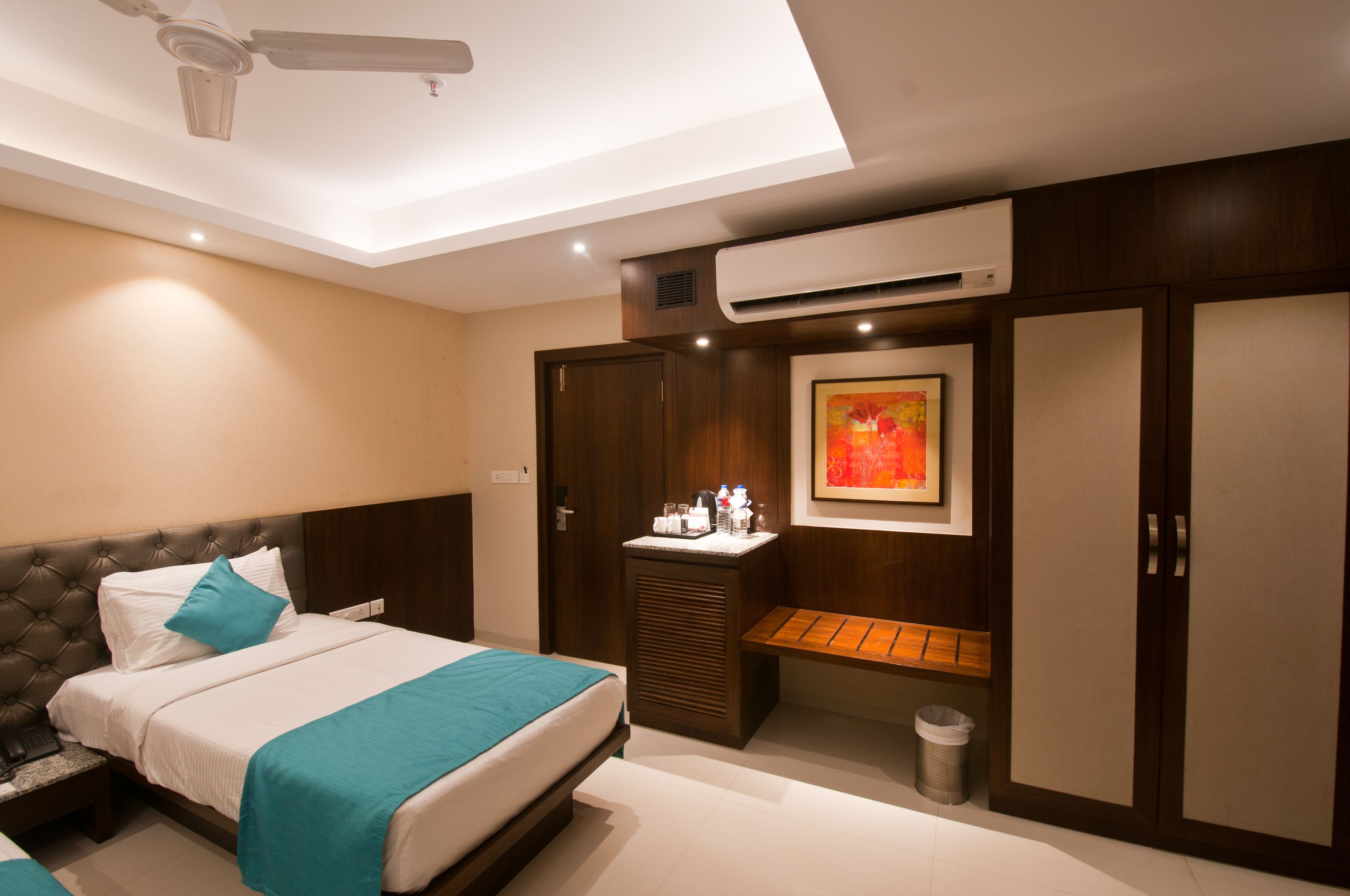 A modern hotel room with a bed, a bedside table, a bench, a wardrobe, and an air conditioning unit.