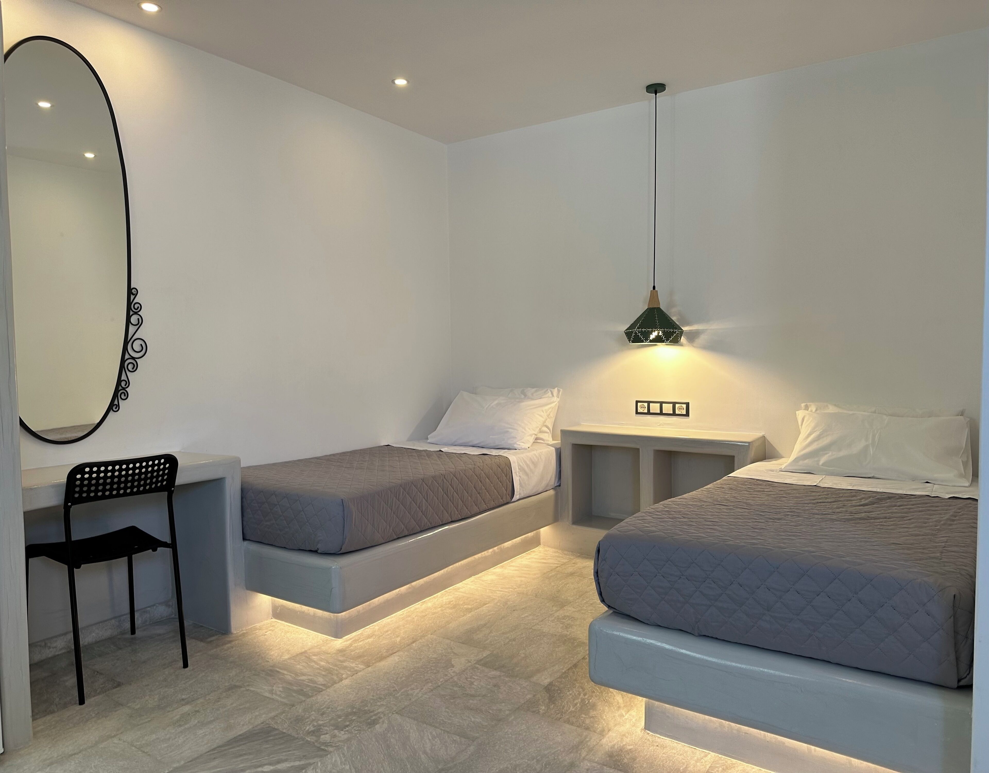 Ein Schlafzimmer mit zwei Betten, einem Spiegel, einem Sessel und einem Nachttisch mit einer Lampe.