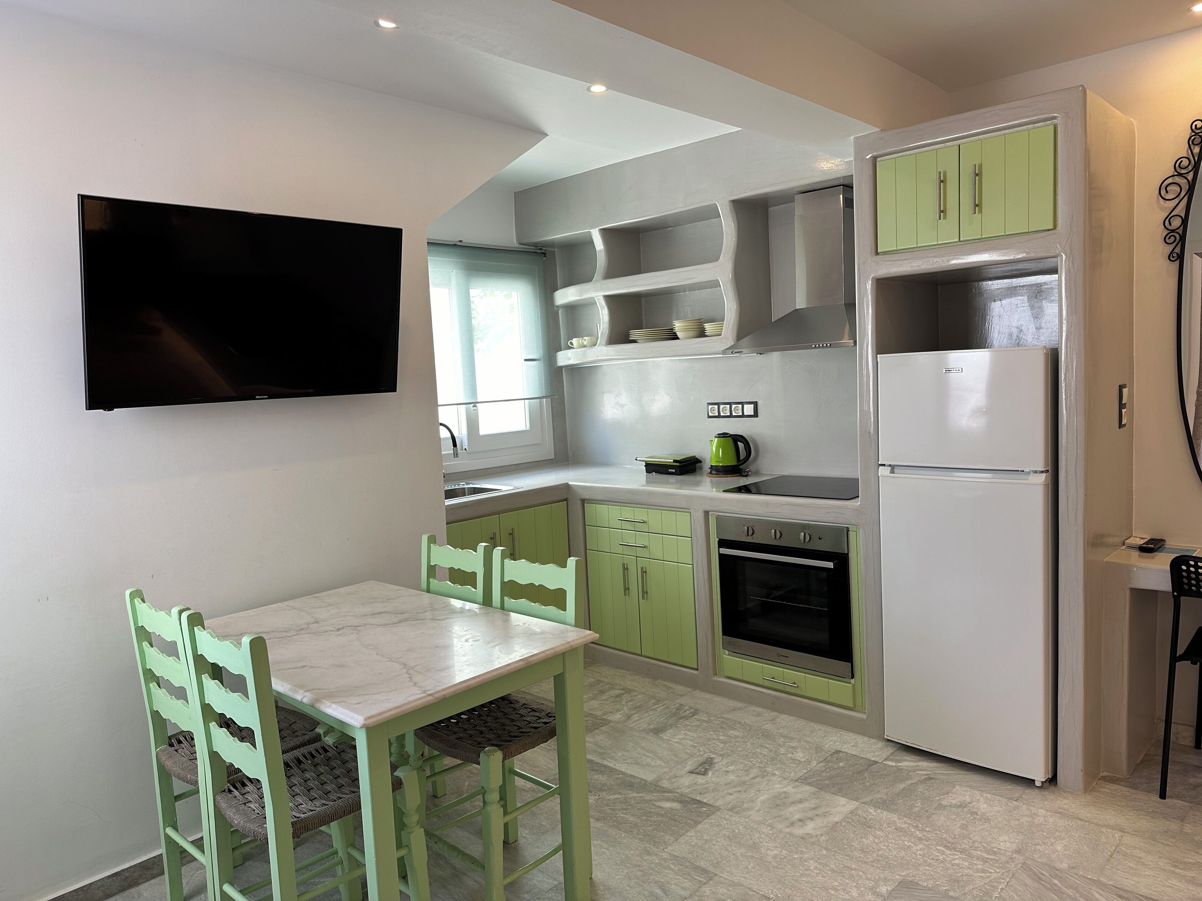 Una cocina compacta con una mesa de comedor, sillas, un televisor montado en la pared y un refrigerador.