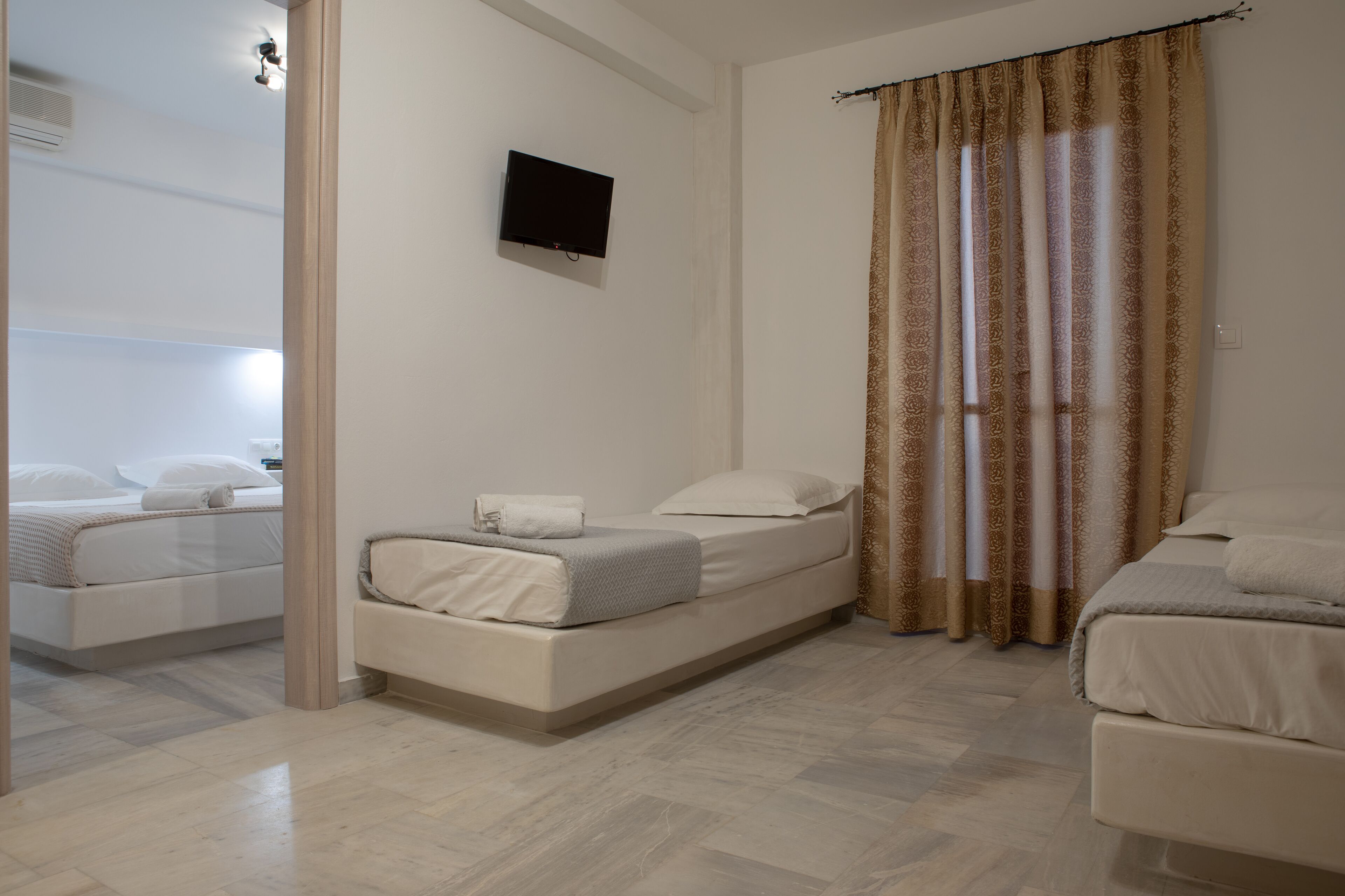 A modern bedroom with two beds, a flat-screen TV, and a large window with patterned curtains.