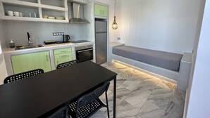 A compact kitchen with a dining table, chairs, a built-in oven, and a refrigerator. - Aphrodite Hotel & Apartments (Ios)