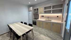 A modern kitchen with a dining table and chairs, built-in cabinets, and a stainless steel sink. - Aphrodite Hotel & Apartments (Ios)