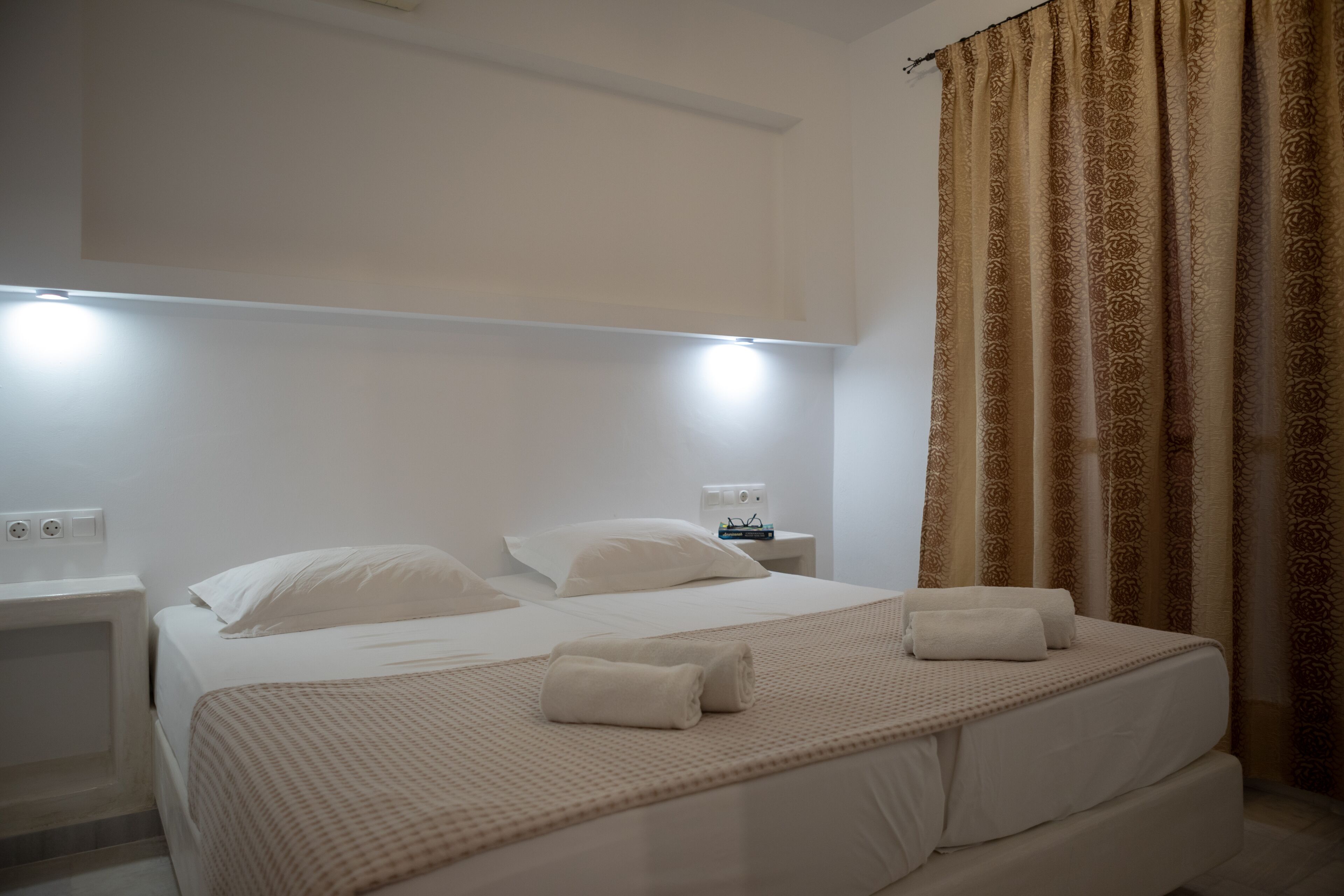A hotel room with a neatly made bed, two bedside tables, and a wall-mounted light fixture.