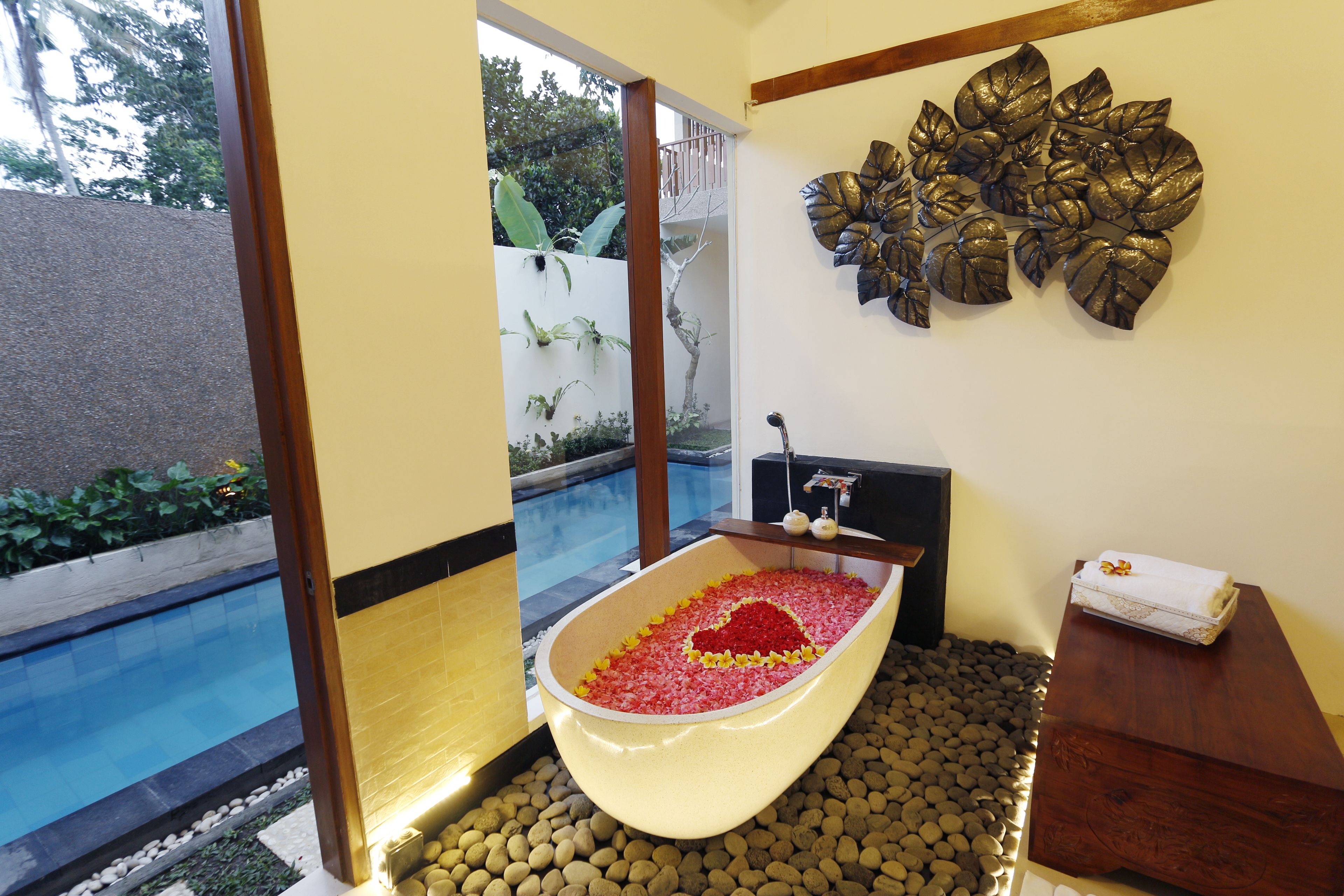 Un área de spa con una bañera llena de pétalos de rosa, un adorno en la pared y vistas a una piscina.