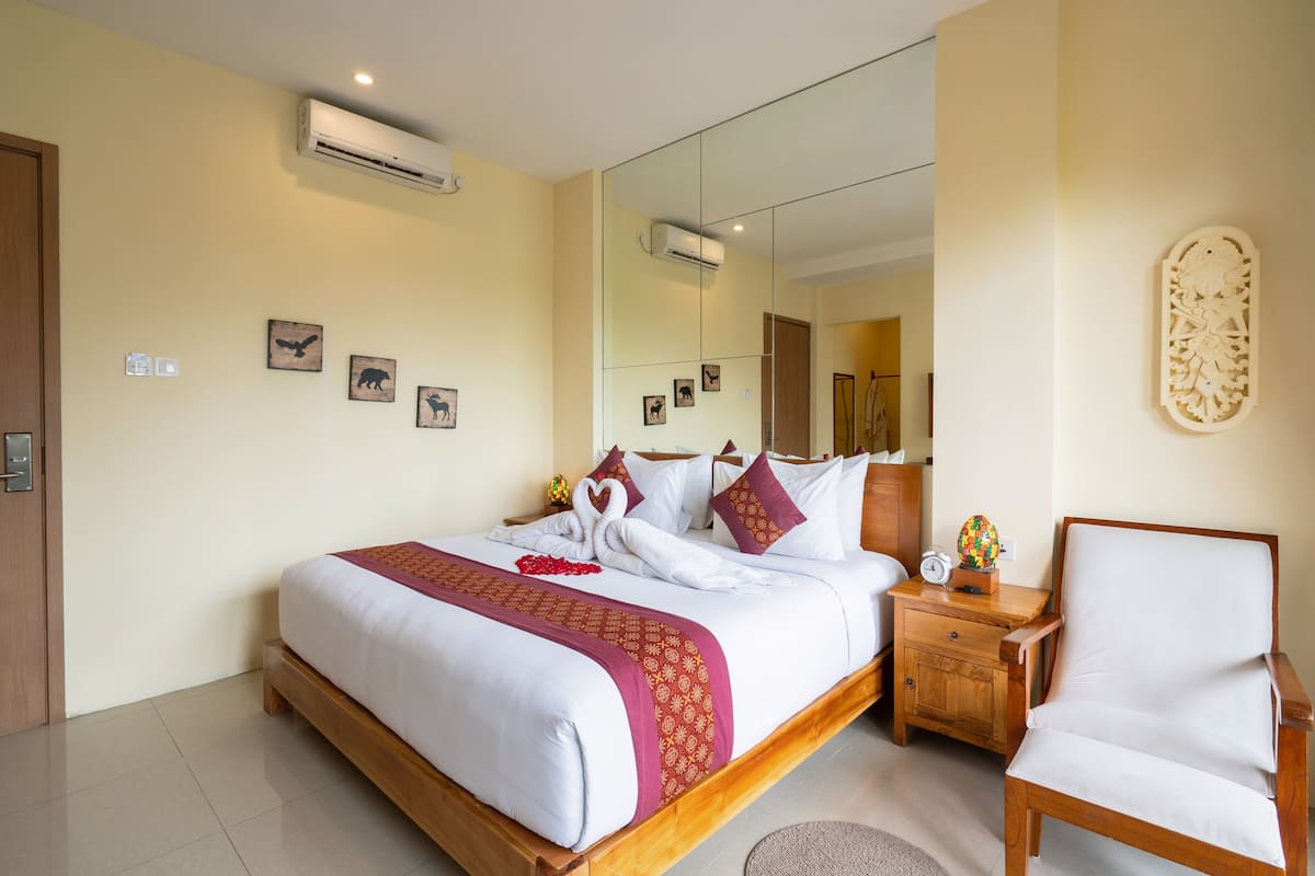 A neatly arranged hotel room with a large bed, a wooden nightstand, a chair, and a mirror.
