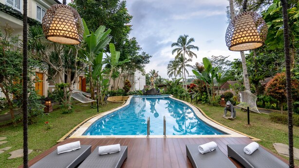 A swimming pool with lounge chairs and a hammock, surrounded by tropical plants and a wooden deck. - Ashoka Tree Resort at Tanggayuda, Ubud (Ubud)