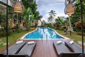 A swimming pool with lounge chairs and a hammock, surrounded by tropical plants and a wooden deck. - Ashoka Tree Resort at Tanggayuda, Ubud (Ubud)